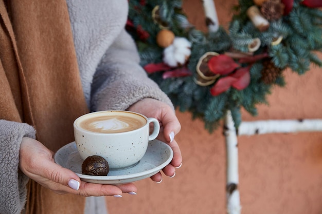 Vrouw met kopje koffie voor stijlvolle kerstkrans buiten Esthetisch gezellig huis