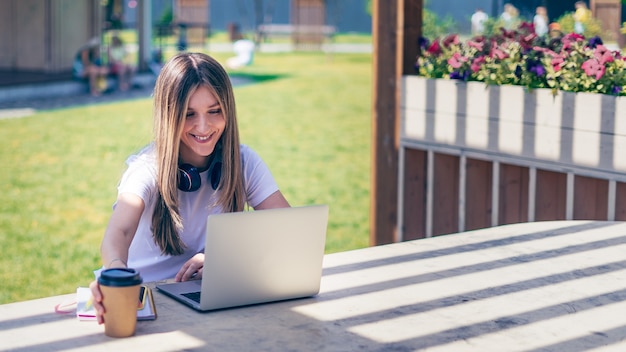 Vrouw met koptelefoon met een videogesprek met laptop buiten in het park blij en lachend meisje aan het werk