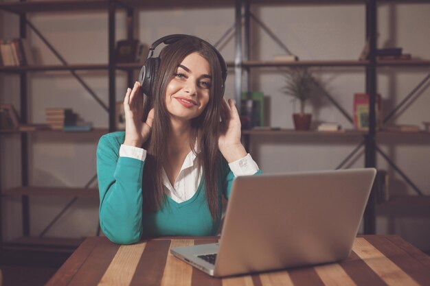 Vrouw met koptelefoon zit aan de houten tafel met laptop