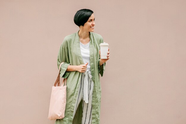 Vrouw met kort haar met herbruikbare koffiekop en eco-tas die van de ochtend geniet.