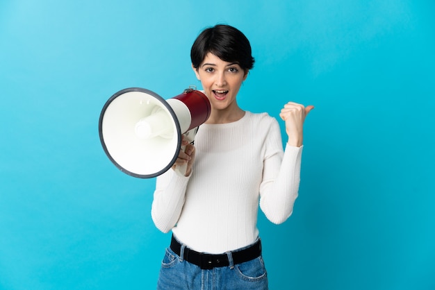 Vrouw met kort haar over geïsoleerde achtergrond die door een megafoon schreeuwt en kant wijst