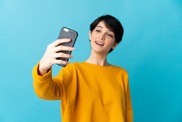 Vrouw met kort haar over geïsoleerde achtergrond die een selfie met mobiele telefoon maakt