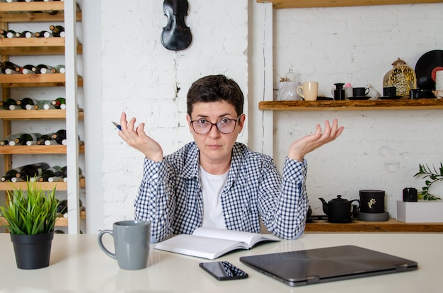 Vrouw met kort zwart haar met bril zit aan de balie in kantoor. steekt onderzoekend zijn handen in de lucht. Emotioneel gezicht