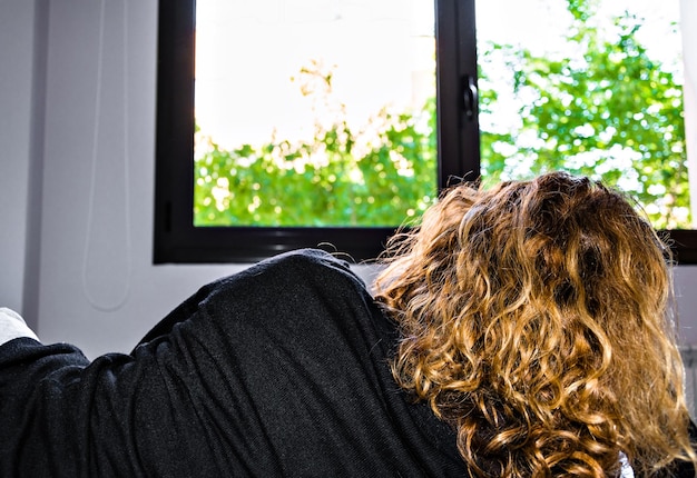 Vrouw met krullend blond haar die in bed ligt en uit het raam kijkt.