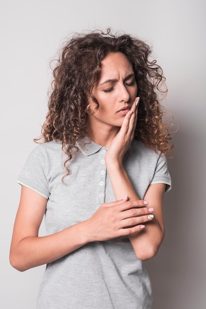 Vrouw met krullend haar die tandpijn hebben tegen grijze achtergrond