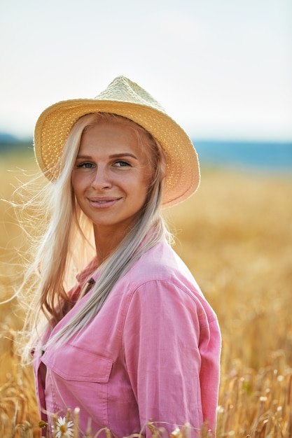 Vrouw met lang blond haar en een strooien hoed in een tarweveld