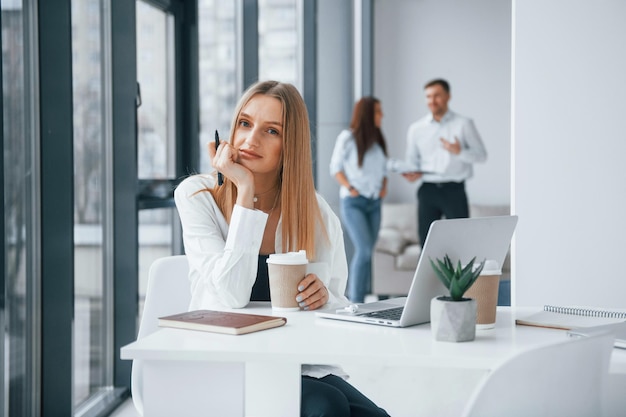 Vrouw met laptop die voor een groep jonge succesvolle teams zit die binnenshuis op kantoor werken en communiceren