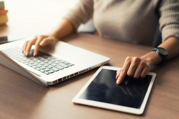 Vrouw met laptop en digitale tablet tijdens het werken op kantoor, handen close-up.