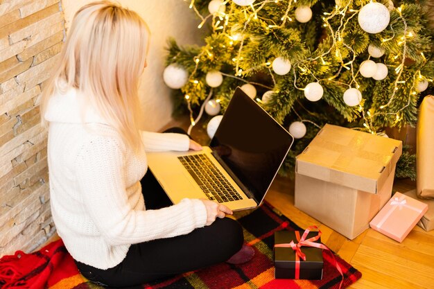 vrouw met laptop op de achtergrond van een kerstboom accepteert online gefeliciteerd merry christmas