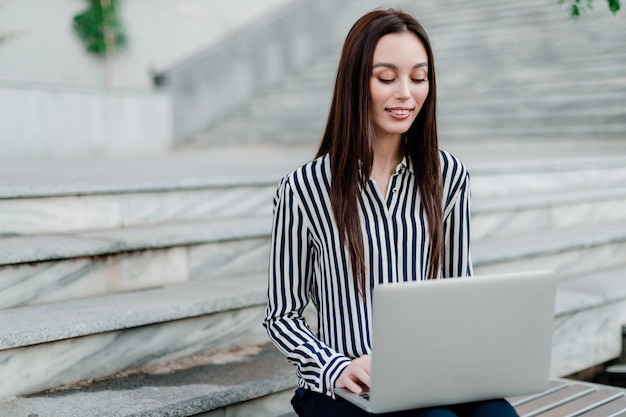 Vrouw met laptop zitting op treden in de stad