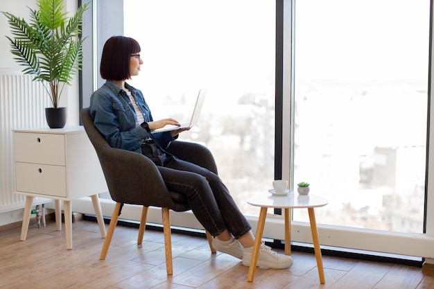 Vrouw met laptopzitting dichtbij venster in bureauleunstoel