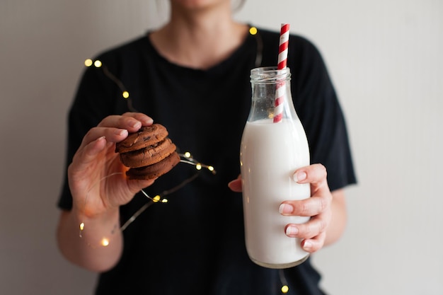 Vrouw met lekkere koekjes en fles verse melk over gloeiende lichten close-up. Winter vakantie seizoen. Goedemorgen.