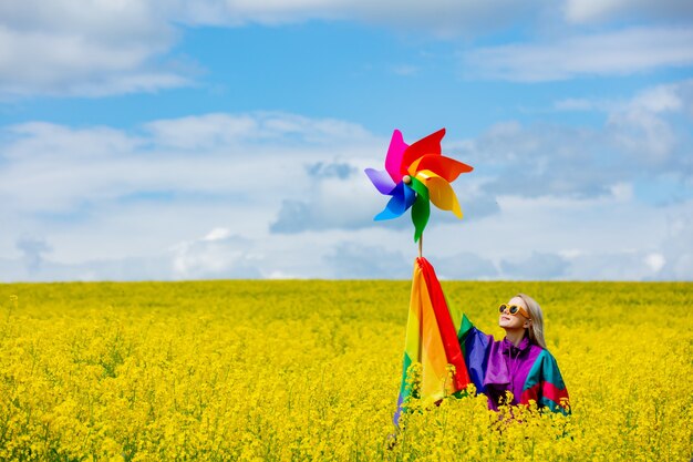 Vrouw met lgbt-regenboogvlag en pinwheel op geel koolzaadveld in het voorjaar