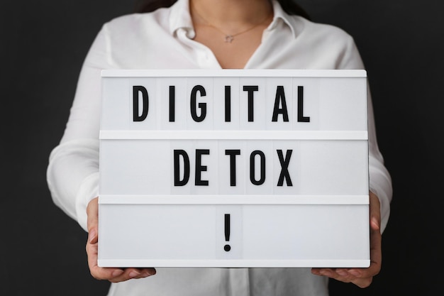 Vrouw met lightbox met zin DIGITAL DETOX op zwarte achtergrond close-up