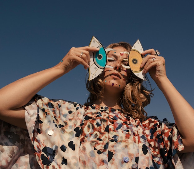 Foto vrouw met make-up die een kartonnen decoratie vasthoudt tegen een heldere lucht