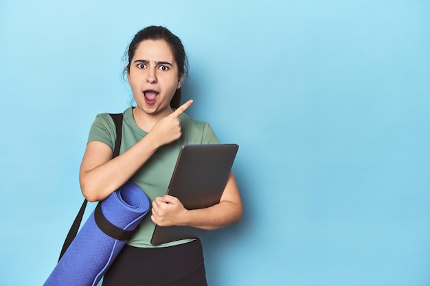 Vrouw met mat en laptop op blauw wijzend naar de zijkant