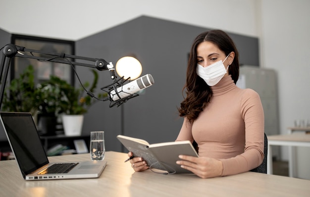 Vrouw met medisch masker in een radiostudio met microfoon en laptop