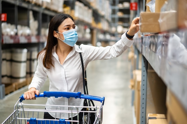 Vrouw met medisch masker kijken en winkelen in het magazijn tijdens coronavirus pandemie