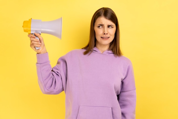 Foto vrouw met megafoon in handen kijkend naar camera met fronsend gezicht met paarse hoodie