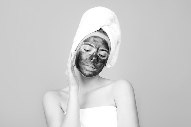 Vrouw met met houtskoolmasker wat betreft haar neus Modder gezichtsmasker gezicht klei masker spa Mooie vrouw met cosmetische modder gezichtsprocedure spa gezondheidsconcept Huidverzorging schoonheidsbehandeling Handdoek op hoofd