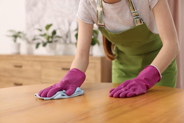 Vrouw met microfiber doek schoonmaakt houten tafel in kamer close-up