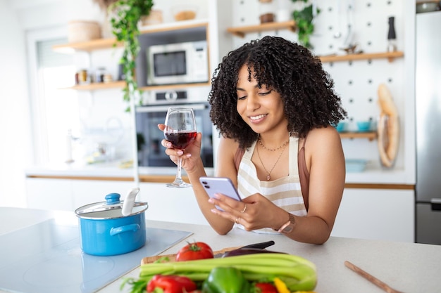 Vrouw met mobiele telefoon en een glas wijn in de keuken thuis