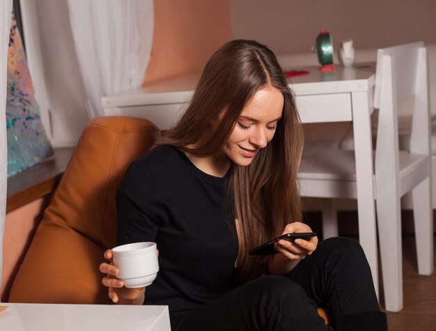 Vrouw met mobiele telefoon en kopje koffie