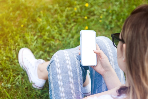 Vrouw met mobiele telefoon met leeg scherm in haar hand. grasruimte, zonnestralen.