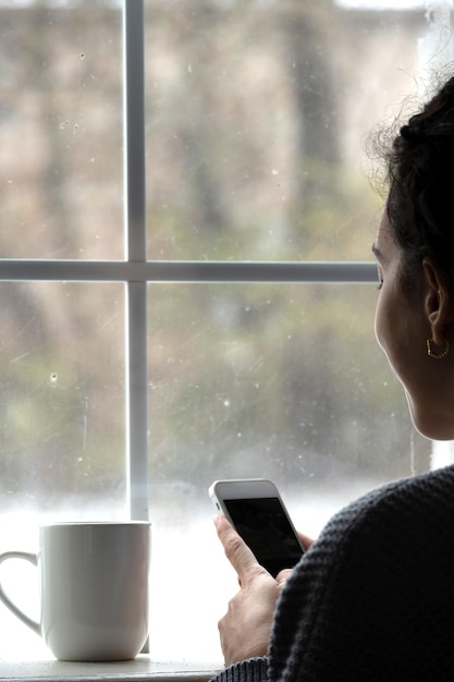 Foto vrouw met mobiele telefoon voor het raam met sneeuw