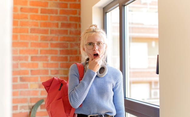 Vrouw met mond en ogen wijd open en hand op kin, die zich onaangenaam geschokt voelt, zegt wat of wauw