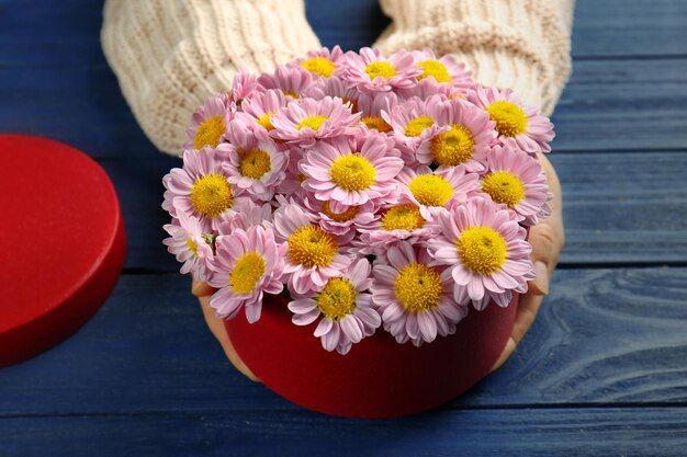 Vrouw met mooie bloemen in geschenkdoos op houten achtergrond