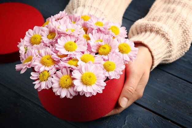 Vrouw met mooie bloemen in geschenkdoos op houten tafel