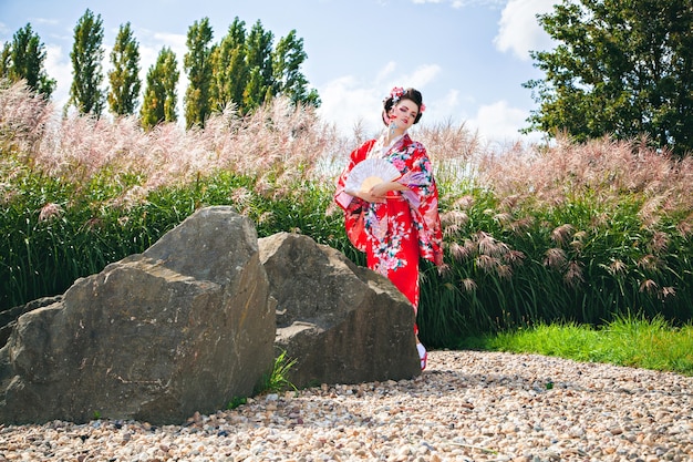 Vrouw met mooie make-up als Japanse Geisha in tuin met fan