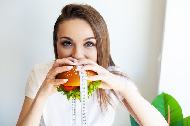 Vrouw met ongezonde hamburger en meetlint gewichtsverlies concept