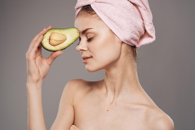Vrouw met ontblote schouders avocado in handen bijgesneden uitzicht over grijze achtergrond
