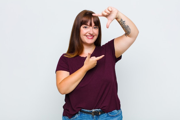 Vrouw met overgewicht die zich gelukkig, vriendelijk en positief voelt, lacht en een portret of fotolijst met handen maakt