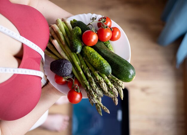 vrouw met overgewicht in de keuken met meetlint centimeter op taille buikvet vasthouden met handvrouw