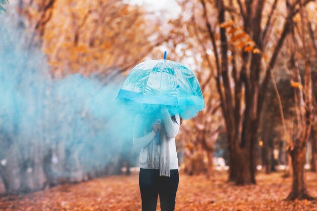 Foto vrouw met paraplu en noodflare die in de herfst in het park staat