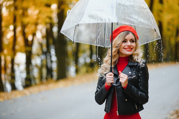 Foto vrouw met paraplu wandelen in de regen in prachtig herfstpark.