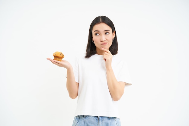 Vrouw met peinzende gezichtsholding cupcake en het denken witte achtergrond