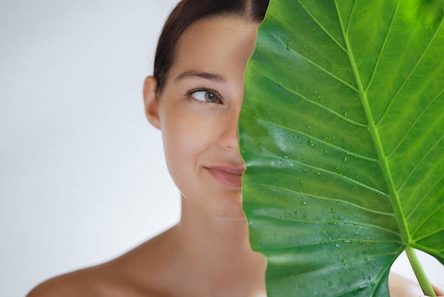 Vrouw met perfecte naakte make-up stralende huid en een stralende glimlach achter groot blad