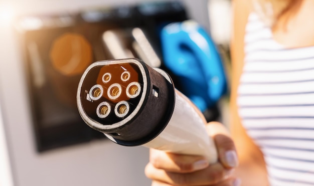 Vrouw met plug-oplaadkabel op een laadstation voor elektrische auto's. Milieuvriendelijk alternatief energieconcept