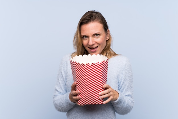 Vrouw met popcorns over geïsoleerde blauwe muur