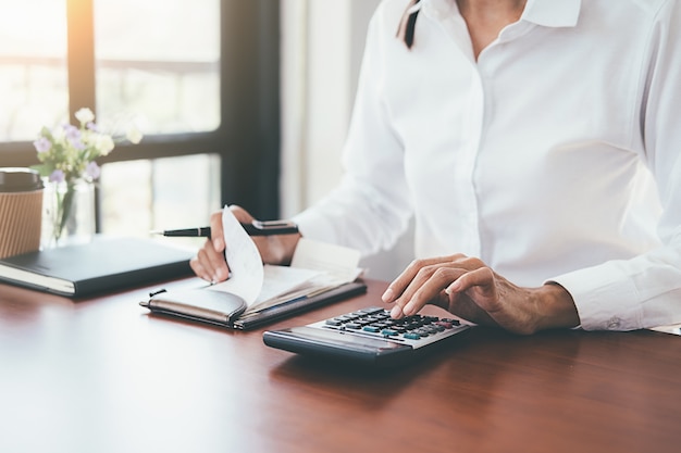 Vrouw met rekeningen en calculator. Vrouw die calculator gebruikt om rekeningen bij de lijst in bureau te berekenen.