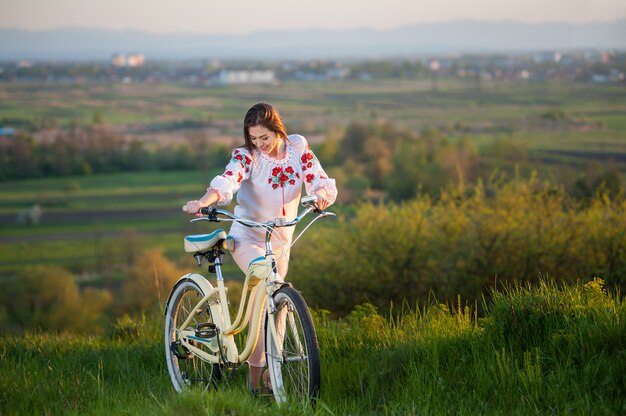 Vrouw met retro fiets op de heuvel in de avond