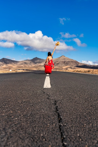 Vrouw met rode koffer op een verlaten weg in het dorre landschap.