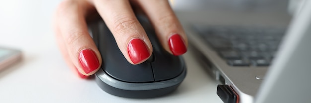 Vrouw met rode manicure met computermuis in de buurt van laptop close-up
