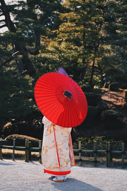 Vrouw met rode paraplu die op de weg tegen bomen staat