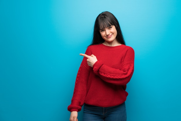 Vrouw met rode trui over blauwe muur wijzend naar de kant om een product te presenteren