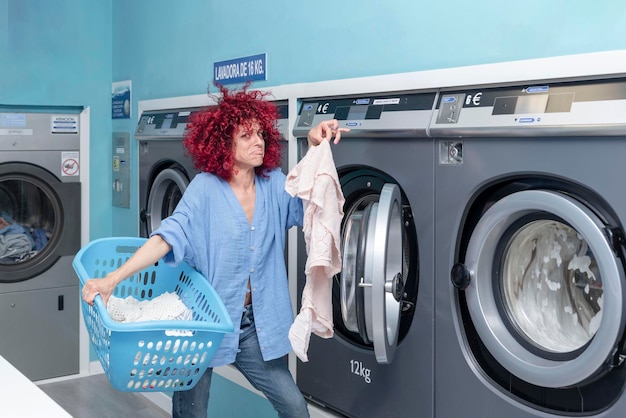 vrouw met rood afrohaar die vuile kleren uit de was haalt in een blauwe automatische wasserette